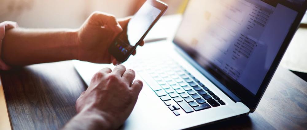 Kontaktieren Sie uns für eine individuelle Beratung durch das Filmunternehmen Berlin Mitarbeiter sitzt im Filmunternehmen Berlin am Laptop mit dem Handy in der Hand und ist bereit für Anrufe von Kunden