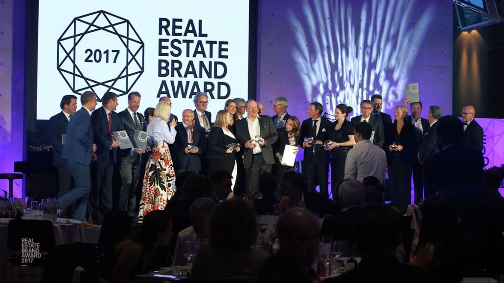 Auf dem Bild sind in der Totalen alle Teilnehmer des Real Estate Brand Awards 2017 auf einer Bühne zu sehen im Rahmen der Event-Dokumentation.