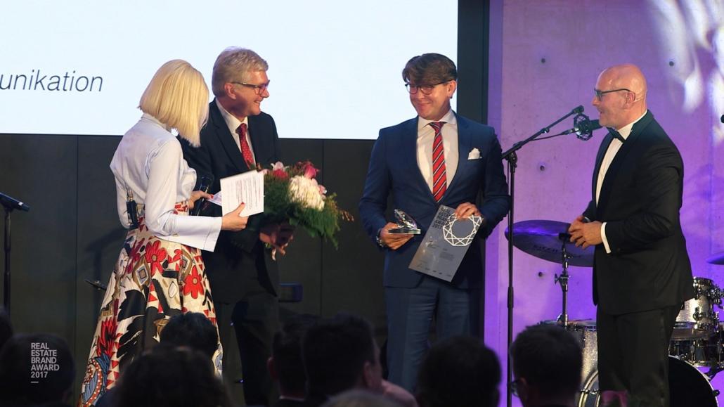 Dargestellt ist auf diesem Bild in Halbtotalen die Preisverleihung eines Event-Teilnehmers, welcher eine Urkunde sowie den Preis in Form eines Diamanten in Händen hält.