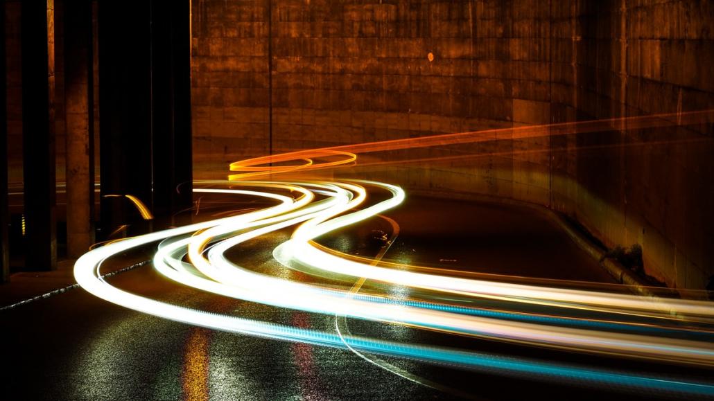 Auf dem Bild sehen wir auf einer Straße bei Nacht Lichtspuren in orangen und türkisen Farbtönen im Rahmen einer Langzeitbelichtung, welche für Imagefilme zum Einsatz kommen können.