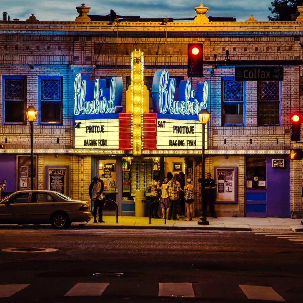 In einem US-amerikanischen Kino die besten Filme aller Zeiten sehen. Um die besten Filme aller Zeiten zu sehen, empfiehlt sich ganz besonders ein Kino dieser Art: Es ist abends und von einer Straße aus sehen wir den Eingang eines US-amerikanischen Kinos. Auf einer typisch beleuchteten Anzeigetafel sind die Filmtitel “Protoje” und “Raging Fyah” in Großbuchstaben abgebildet und darüber in blauer beleuchteter Schreibschrift der Name des Kinos “Bluebird”. Vor dem Kino stehen mehrere Menschen in einer Schlange.